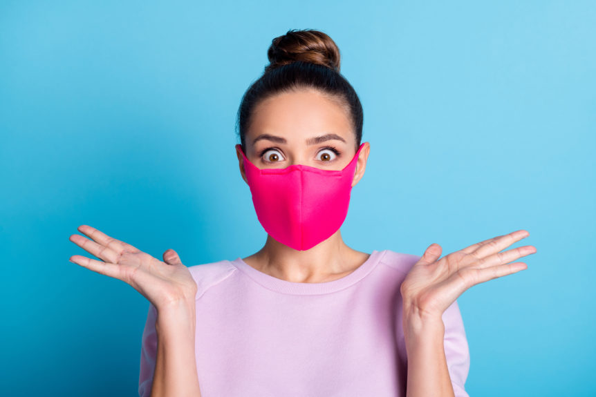 Überraschte Frau mit rosa Mundschutz vor blauem Hintergrund.