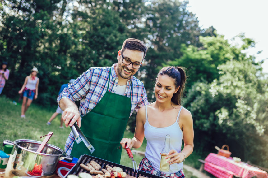 Junge Freunde grillen gemeinsam Fleisch und Gemüse und feiern eine Grillparty.