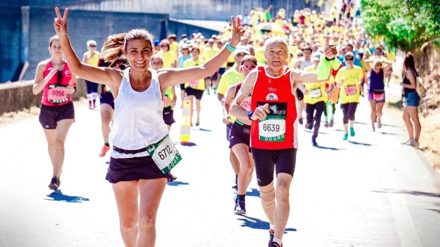 Läufergruppe beim Firmenlauf in Sportshirts mit Startnummern, jubelnde Frau und Mann mit Daumen hoch